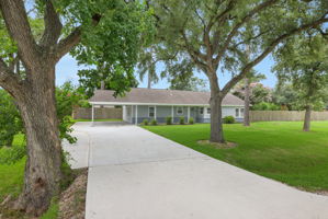 Charming single-story home with a welcoming front yard, mature trees, and a freshly paved driveway. The house features a classic design with a covered carport and is surrounded by a lush green lawn. Perfect for those seeking a serene and picturesque setting.