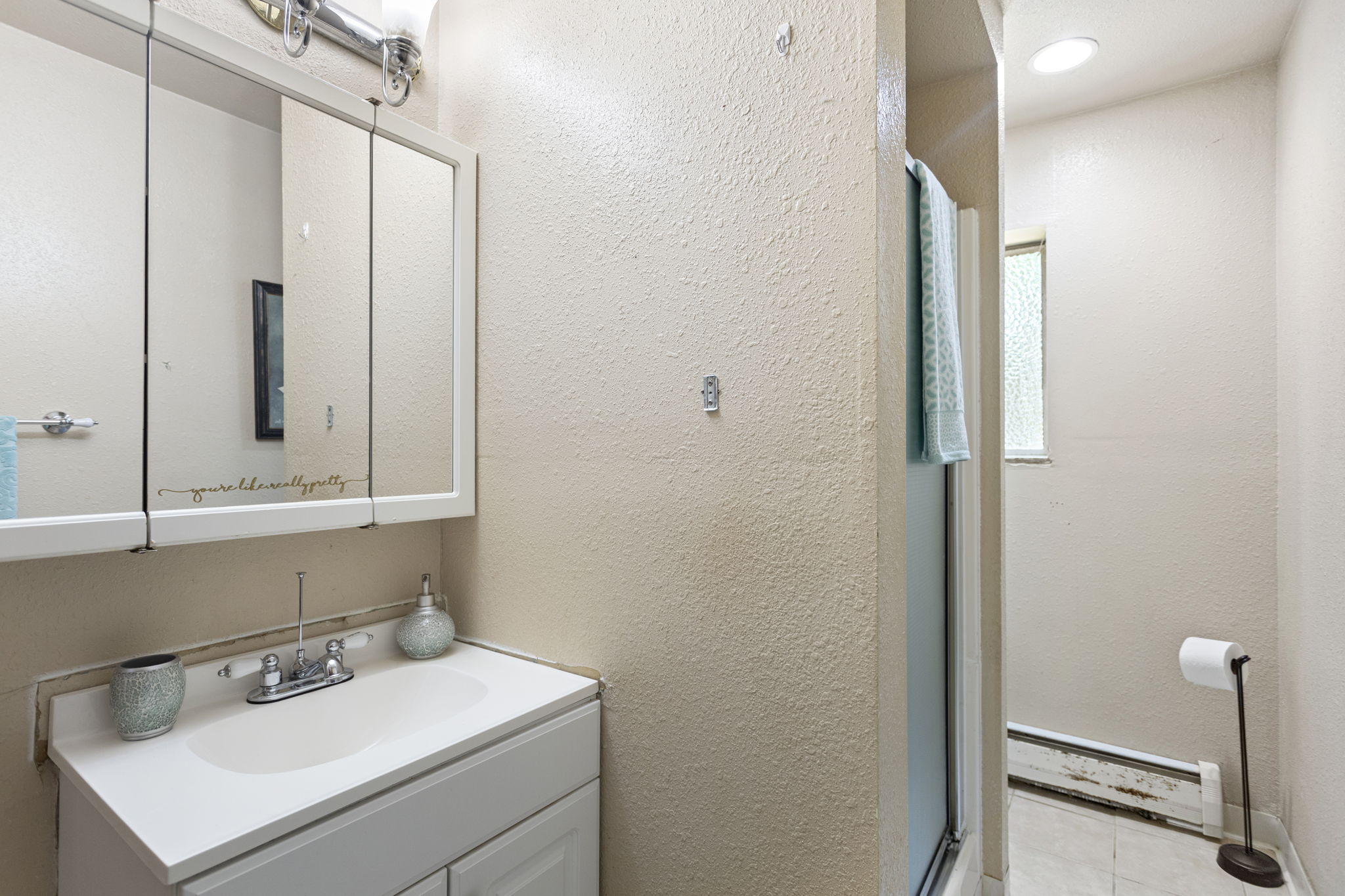 Lower level 3/4 bath — vanity, shower, window. Does its job. Functional, original, yours to improve.