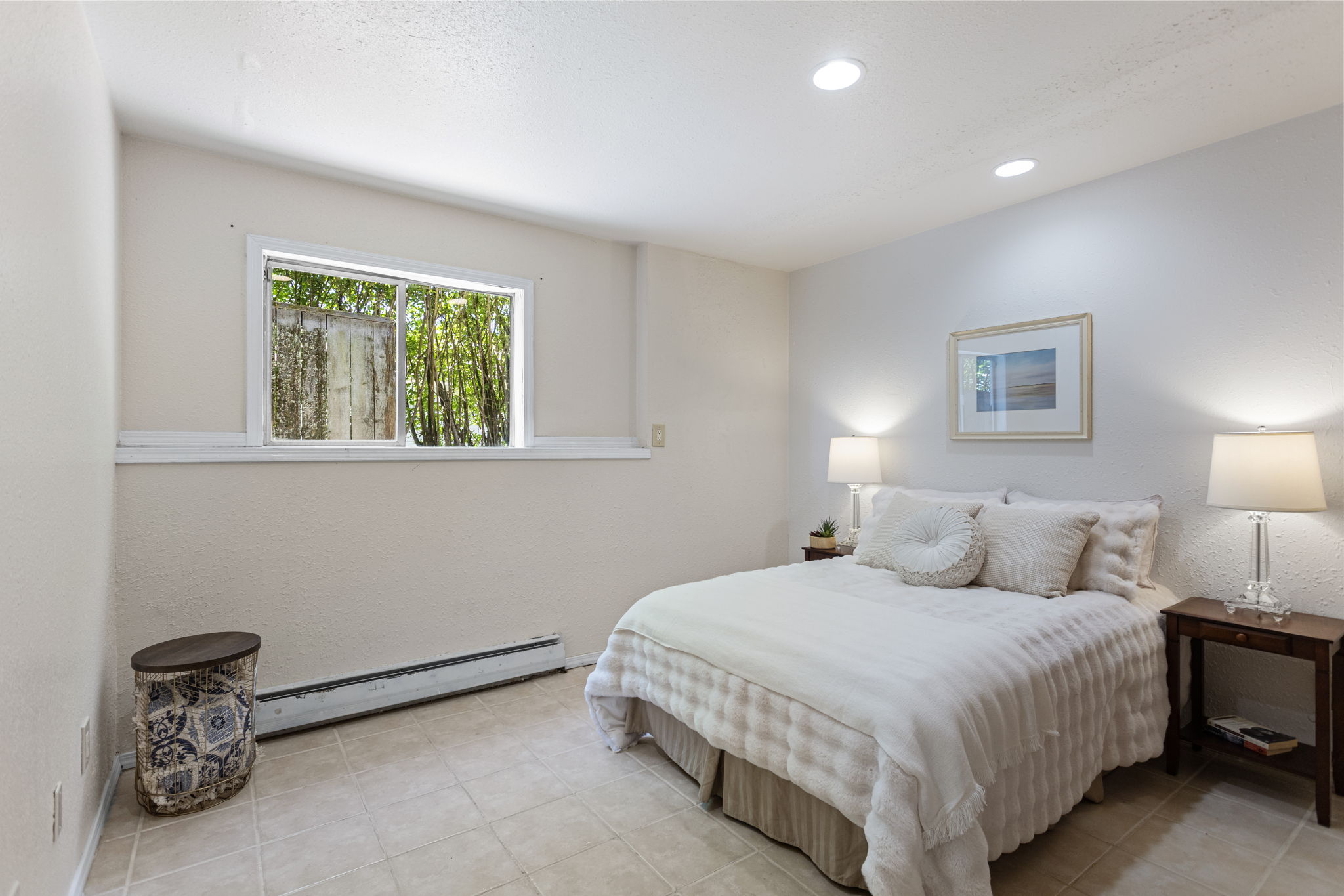 The lower level's private retreat — generous, quiet, and tucked at the back of the house. West-facing window with treetop view, recessed lighting, tile floor. The fifth bedroom that makes the bedroom count feel real.