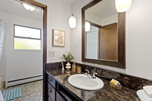 The full bath — granite counter, pendant lighting, mosaic tile floor, tub. Well appointed for its era and ready to serve the whole main floor.
