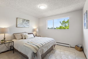 The second bedroom has room for a queen, a west-facing window full of trees, and brand-new carpet underfoot.
