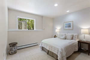 The lower level's private retreat — generous, quiet, and tucked at the back of the house. West-facing window with treetop view, recessed lighting, tile floor. The fifth bedroom that makes the bedroom count feel real.