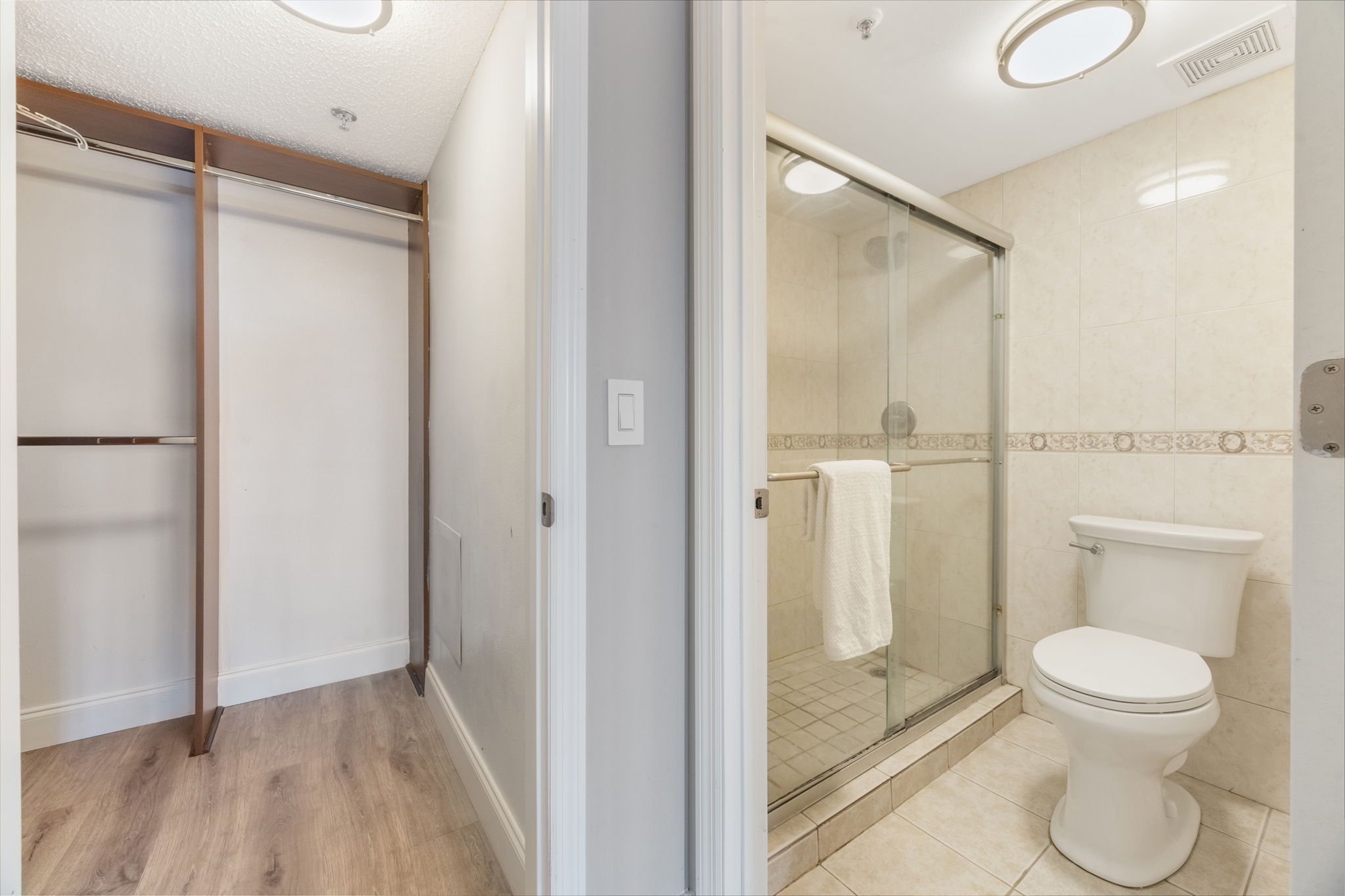Primary glass enclosed shower with privacy door to the right and a partial view of the primary walk-in closet.