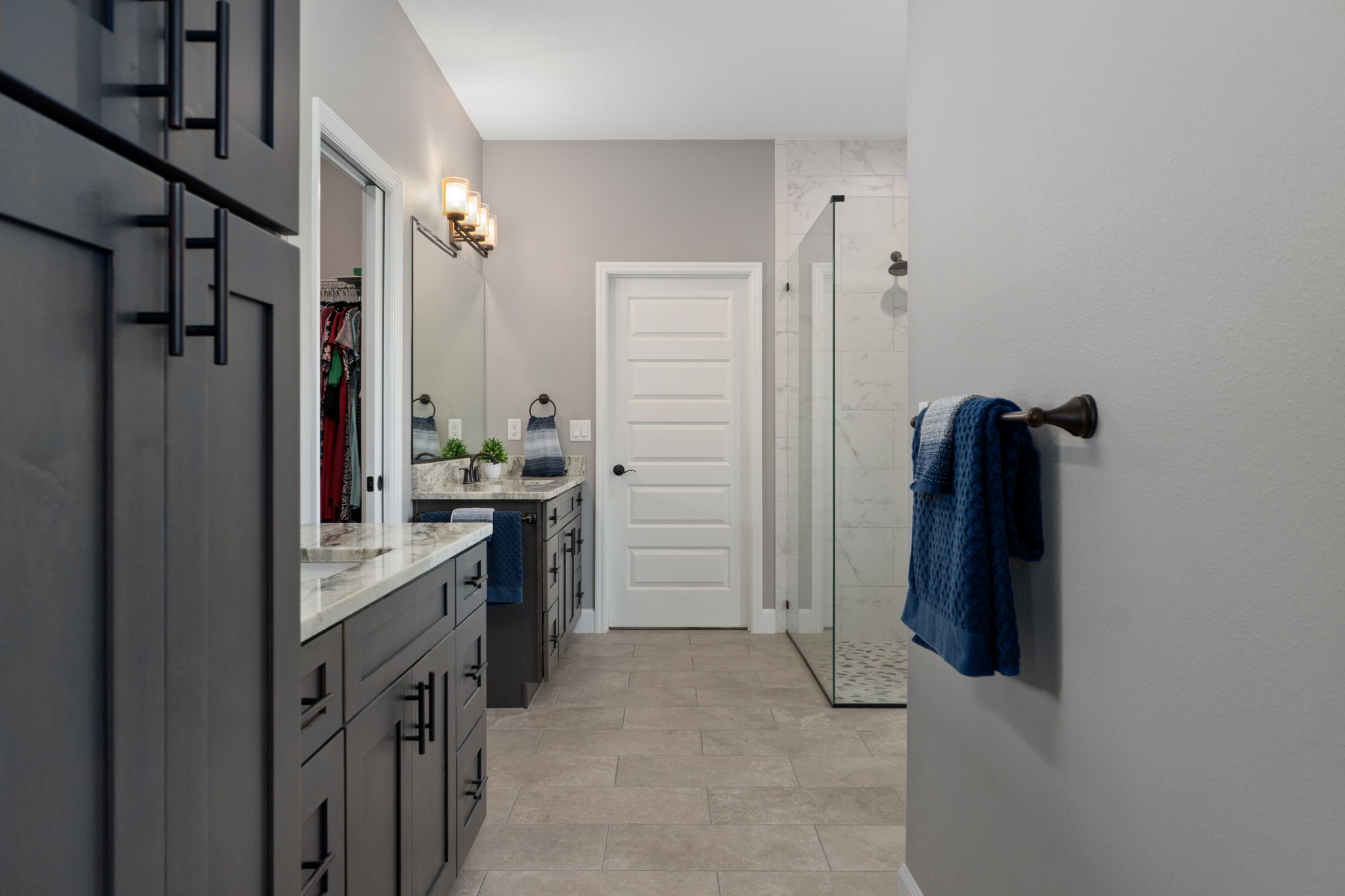 Upon entering the primary bath, there is a built-in cabinet, immediately on the left, perfect for linens or toiletries. The doorway on the left, between the two comfort height vanities is to the walk-in closet.