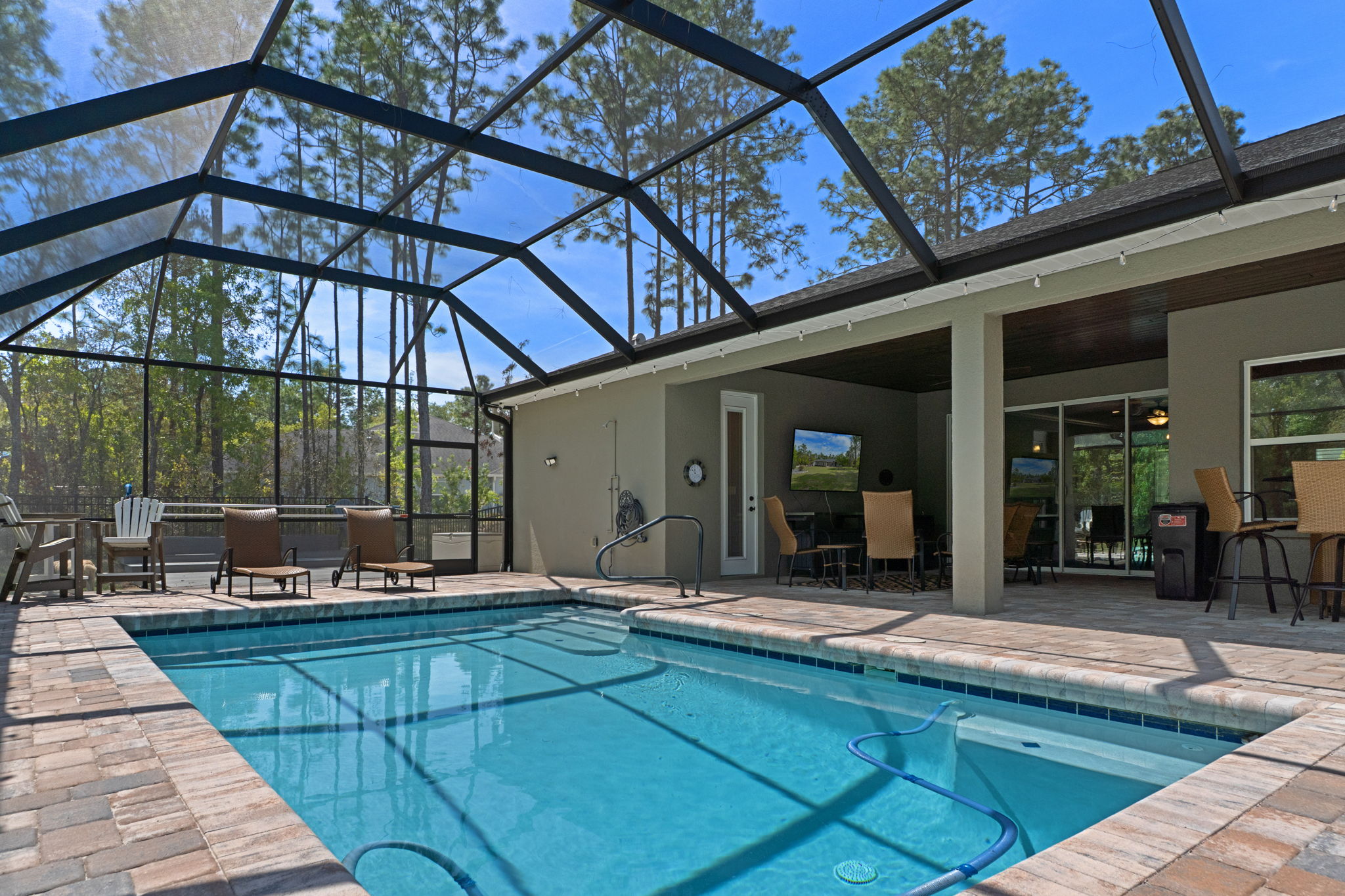 View across pool to the lanai. The door on the left side of the lanai is to the pool bath. It's difficult to see, but there is an outdoor shower to the left of the hose reel on the back wall next to the pool.