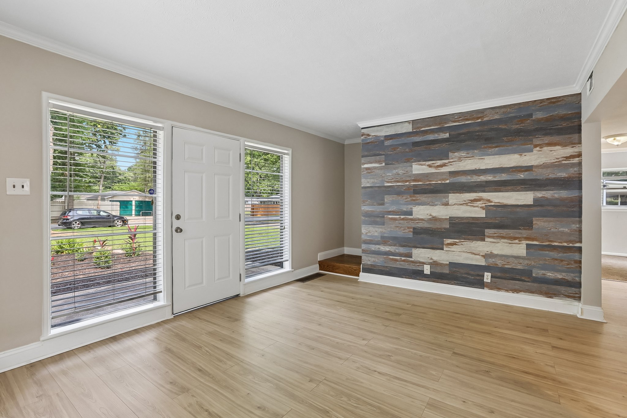 Gather and unwind in a sun-filled living room where warm flooring and a dramatic wood accent wall add instant character.