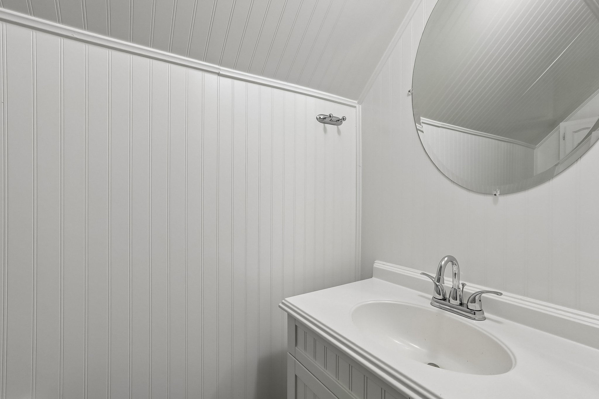 The charming half bath pairs convenient main-level access with beadboard-style detailing and a stylish round mirror.