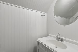 The charming half bath pairs convenient main-level access with beadboard-style detailing and a stylish round mirror.