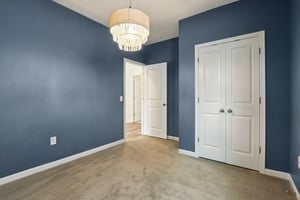 Chic guest bedroom with bold navy walls, stylish chandelier, and double-door closet.