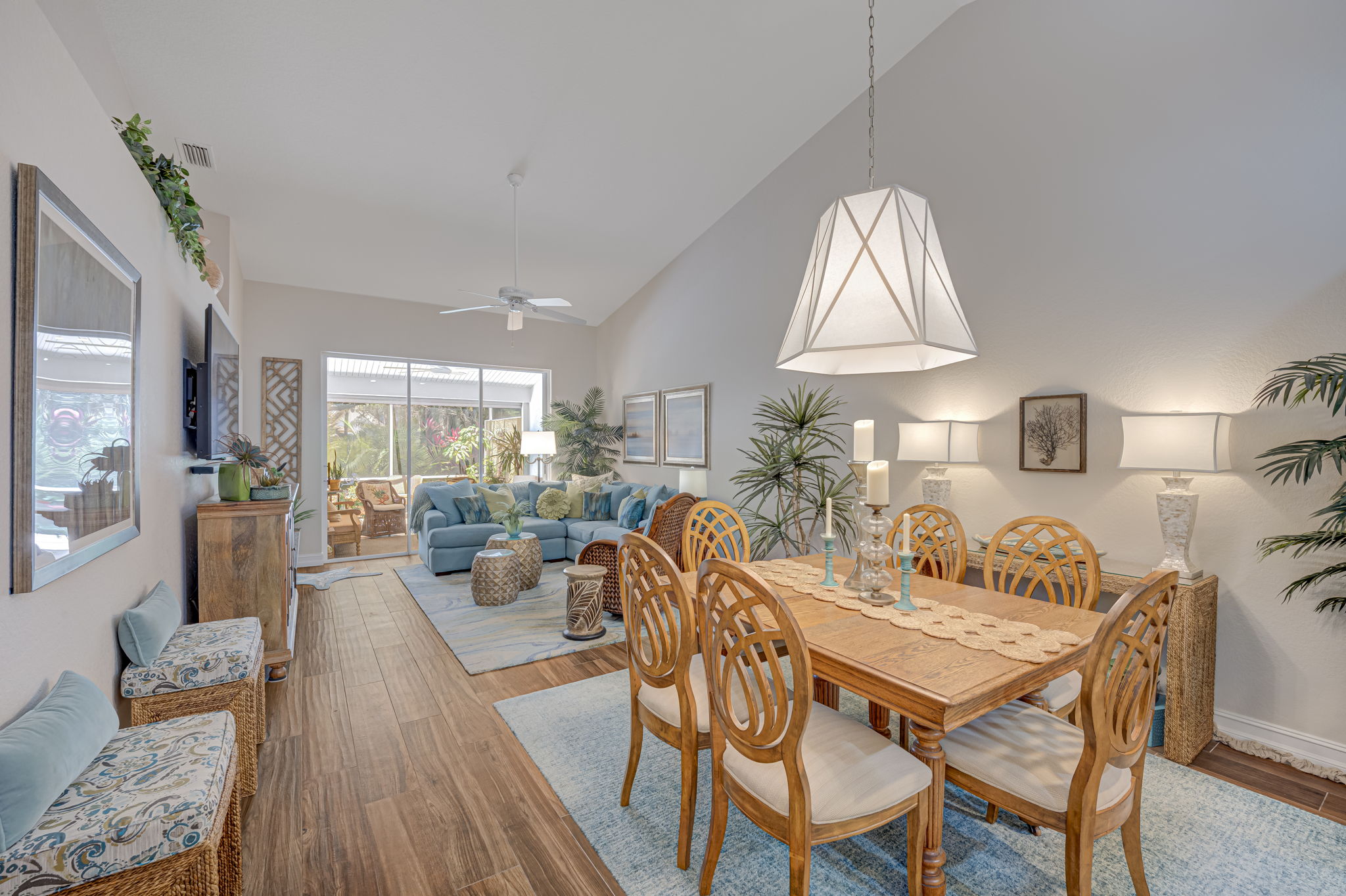 Open-concept great room featuring continuous tile flooring, volume ceilings, and coastal lighting