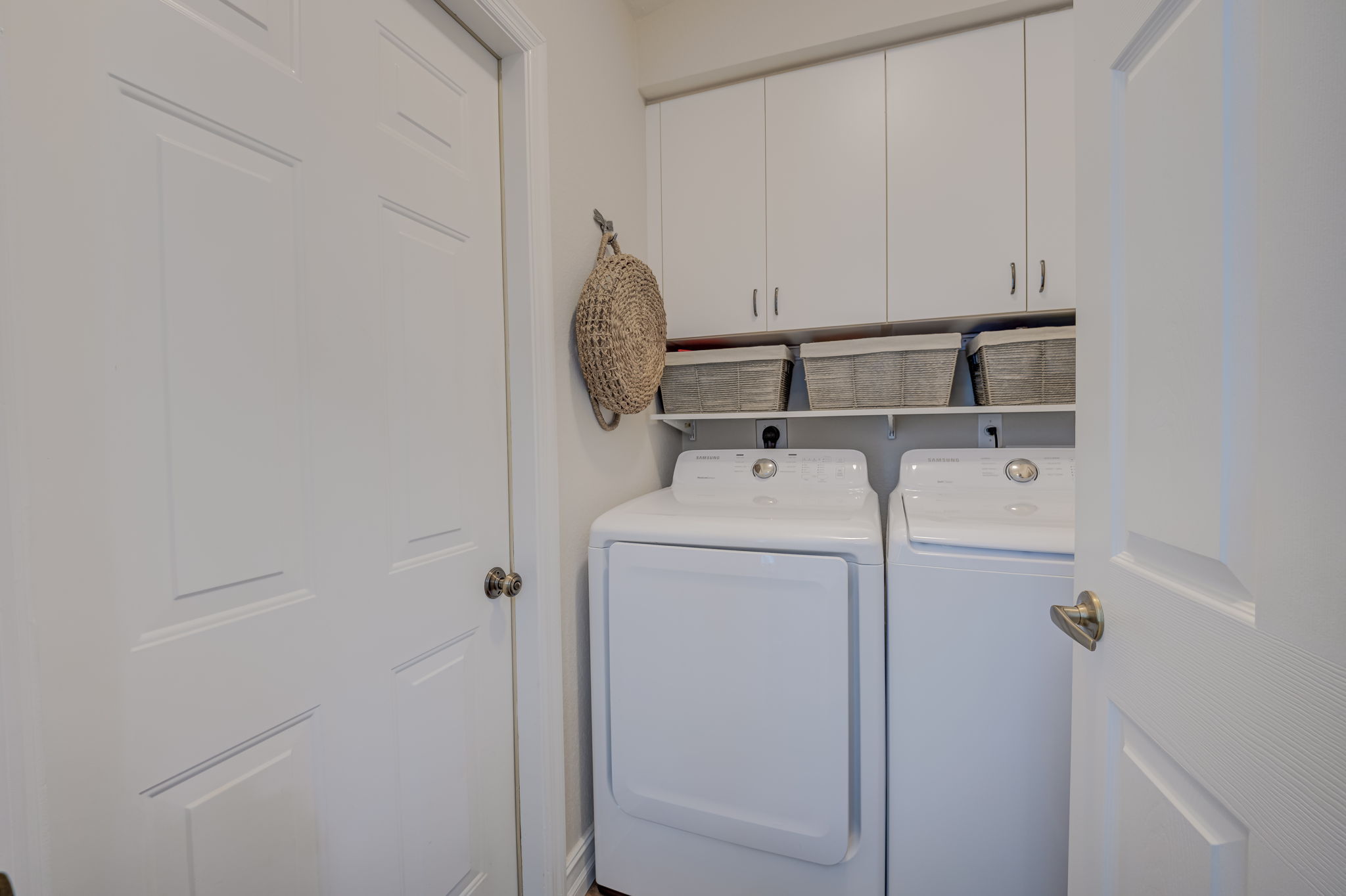 Dedicated interior laundry room equipped with a full-size washer and dryer set, custom overhead cabinetry, and integrated utility shelving