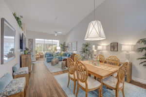 Open-concept great room featuring continuous tile flooring, volume ceilings, and coastal lighting