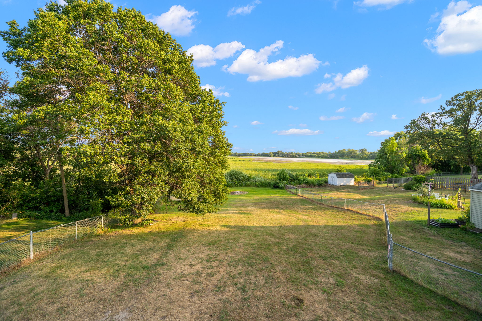 The upper-level deck at 5857 Oneka Lake Boulevard N overlooks the sprawling, fenced-in backyard with Egg Lake in the distance.