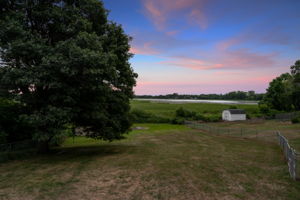 The upper-level deck at 5857 Oneka Lake Boulevard N overlooks the sprawling, fenced-in backyard with Egg Lake in the distance.