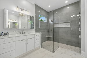 Primary Bathroom with vanity, lighted storage mirror & custom frameless shower & built in niches
