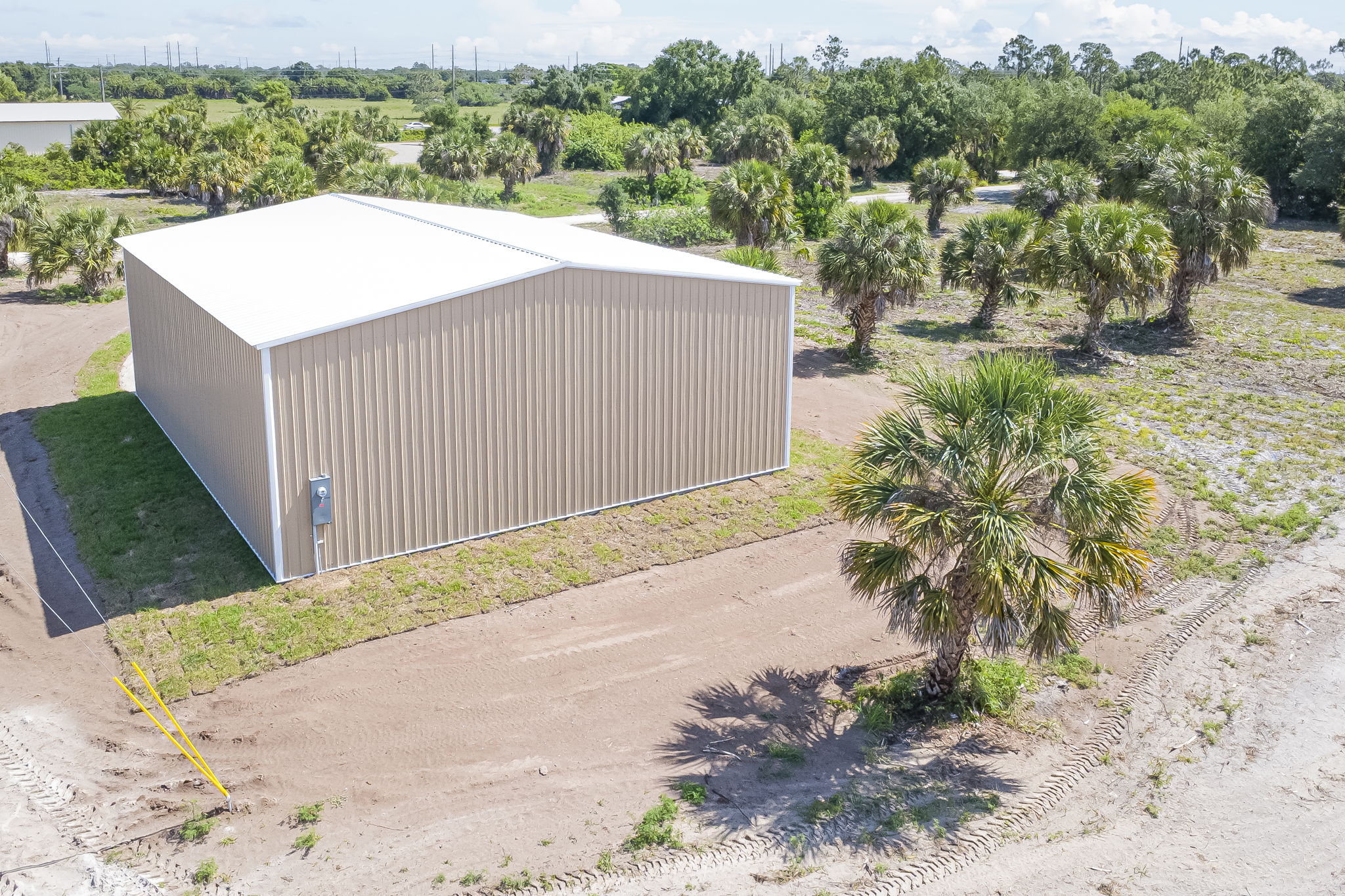 Aerial side view detailing the high-clearance metal roof and the vast, cleared parcel space surrounding the structure.