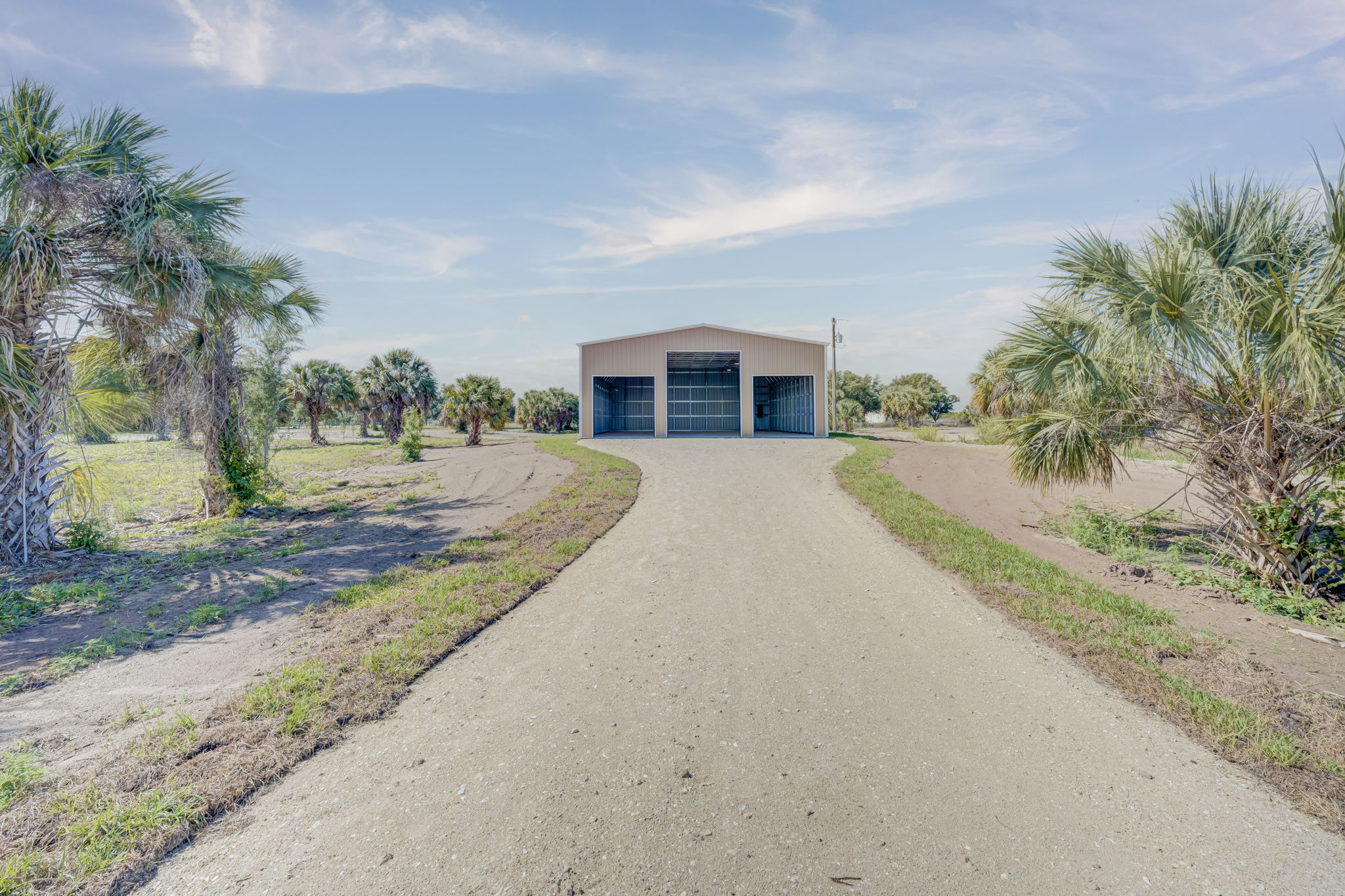 Direct ground-level approach highlighting the well-maintained gravel driveway leading to the custom steel building.