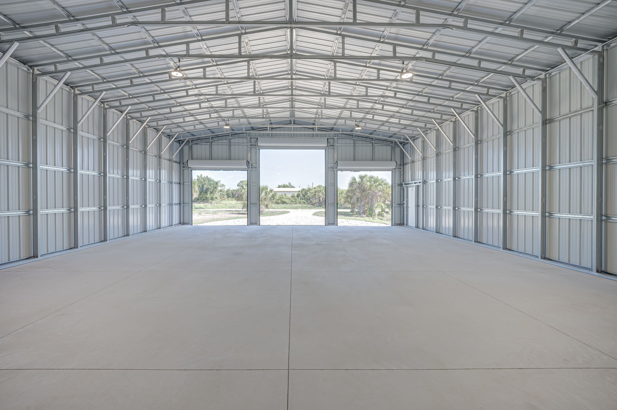 Wide interior view looking out through the open commercial roll-up doors toward the expansive front driveway.
