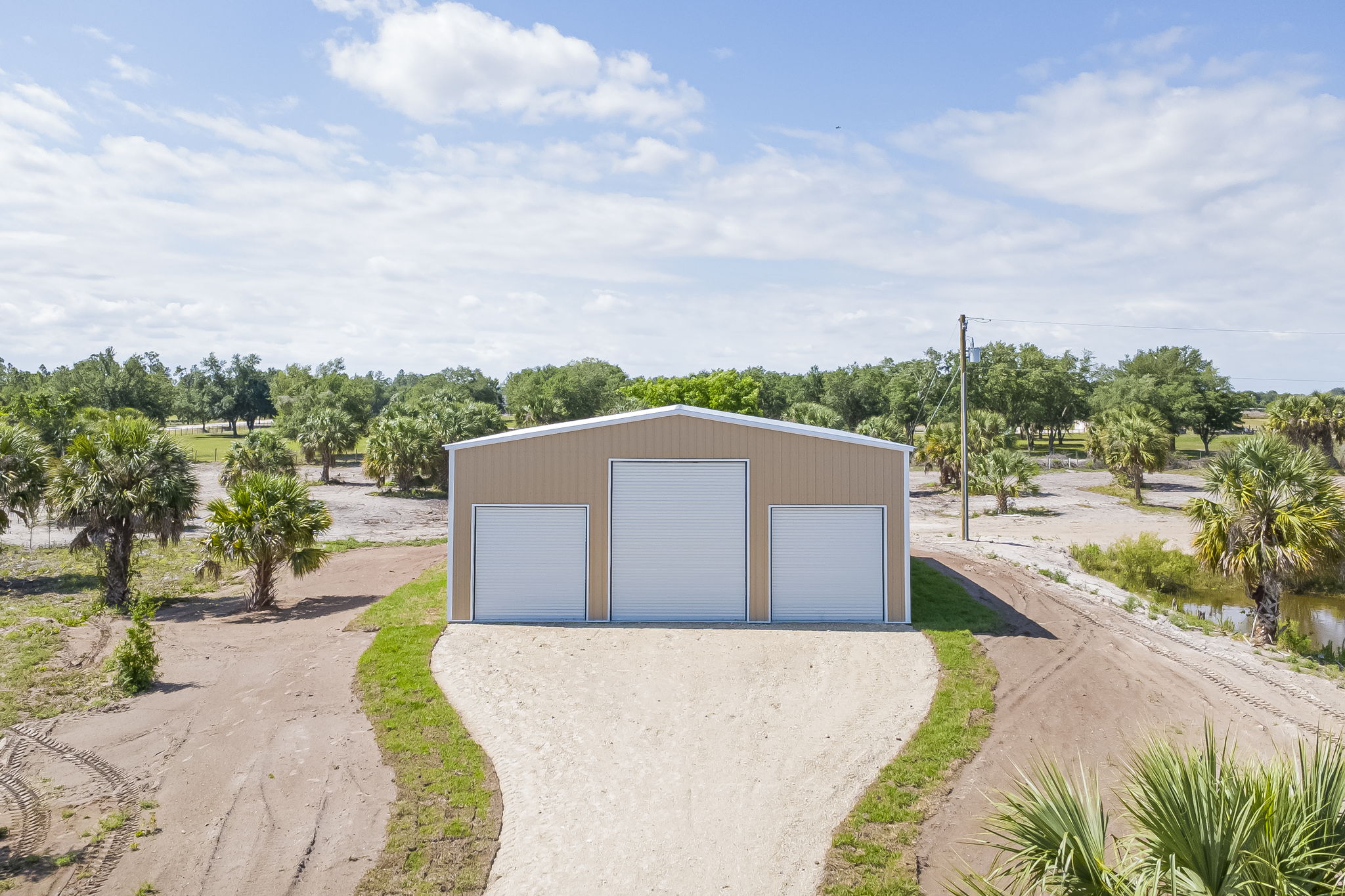 Low aerial view capturing the pristine front facade, dual equipment bays, and expansive gravel parking apron.