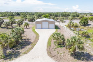 Front aerial perspective of the clear-span steel outbuilding featuring a long, stabilized crushed-shell driveway approach