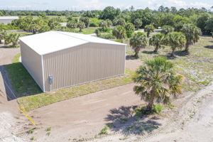 Aerial side view detailing the high-clearance metal roof and the vast, cleared parcel space surrounding the structure.