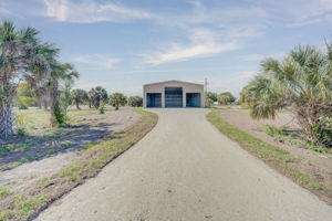 Direct ground-level approach highlighting the well-maintained gravel driveway leading to the custom steel building.
