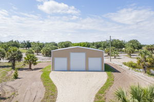 Low aerial view capturing the pristine front facade, dual equipment bays, and expansive gravel parking apron.