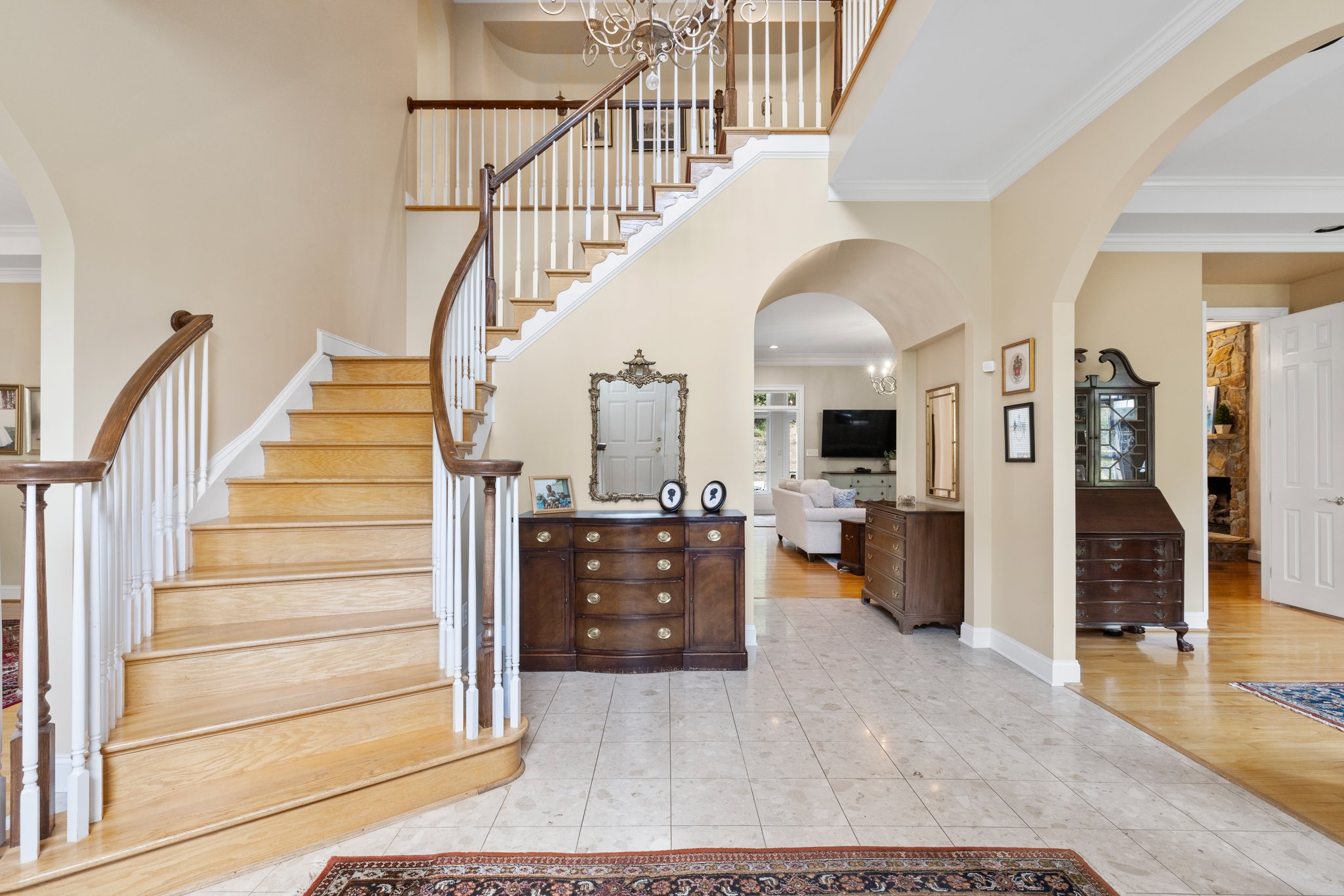 Two story grand foyer with curved staircase, arch openings, and marble tile floors.