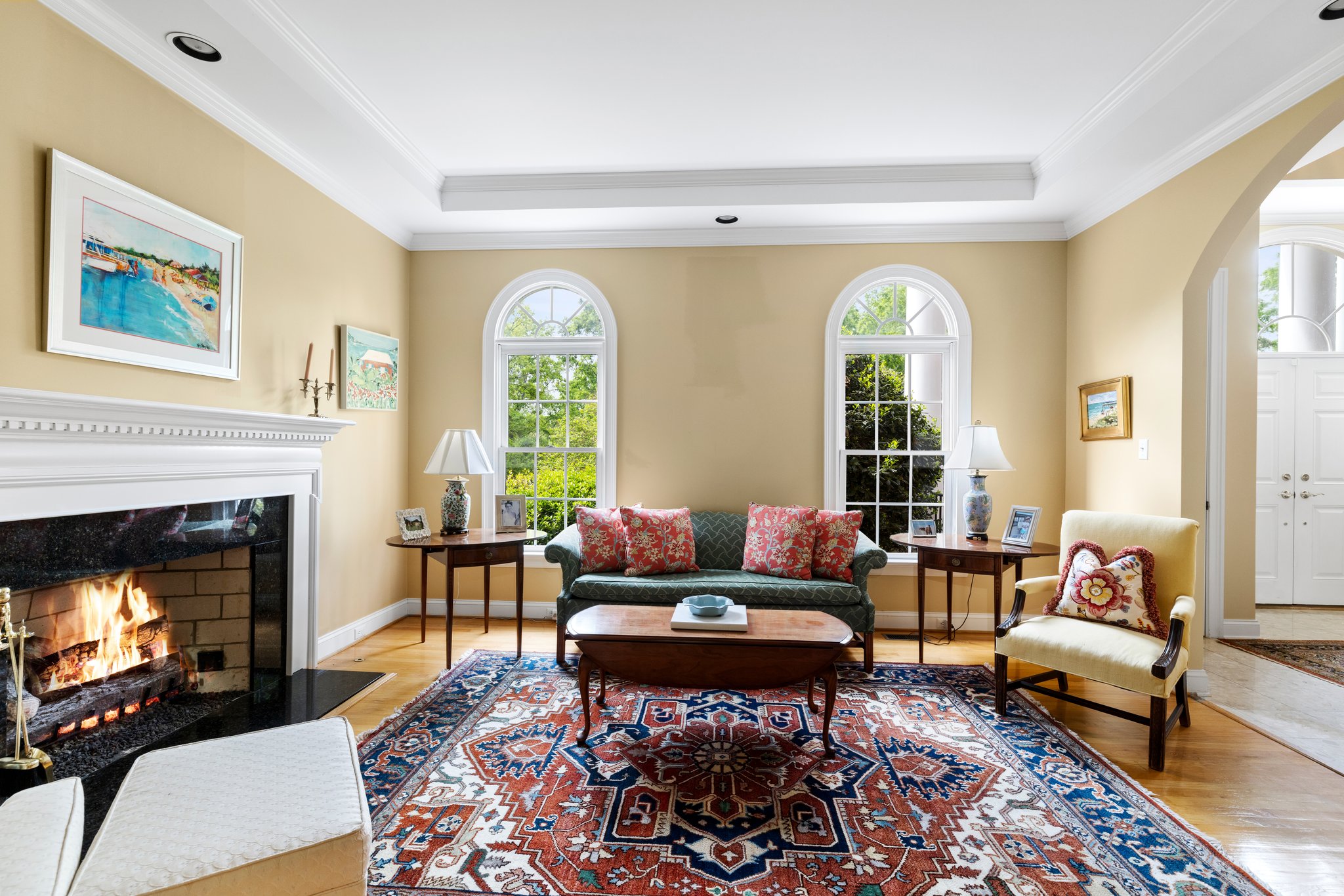 Formal living room with gas fireplace, tray ceiling, arched windows, and hardwood floors.