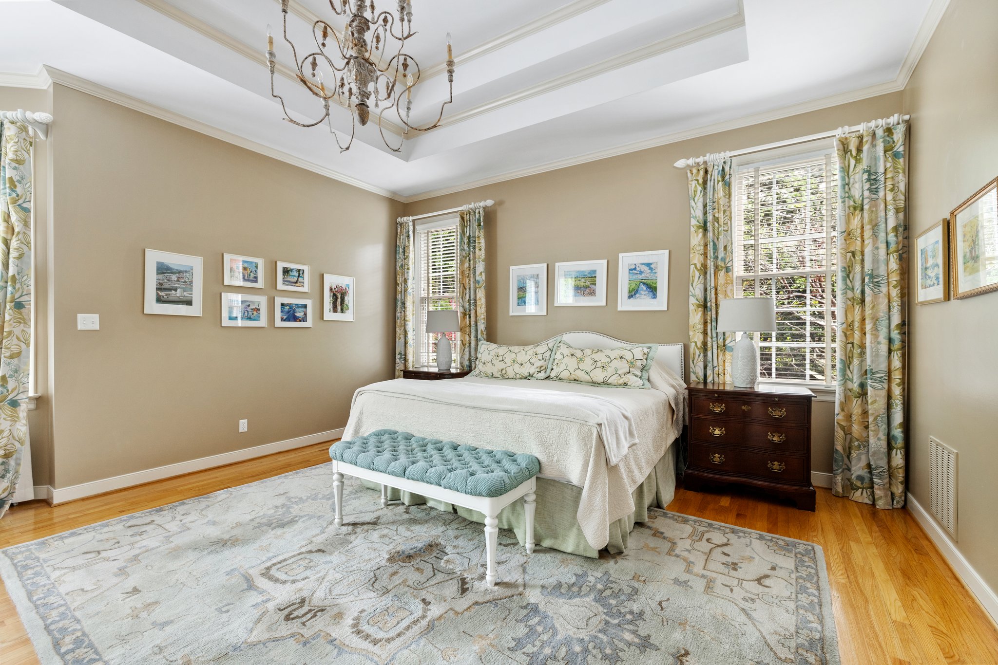 Massive primary bedroom suite with tray ceiling, chandelier, built-in ceiling speakers, and hardwood floors.