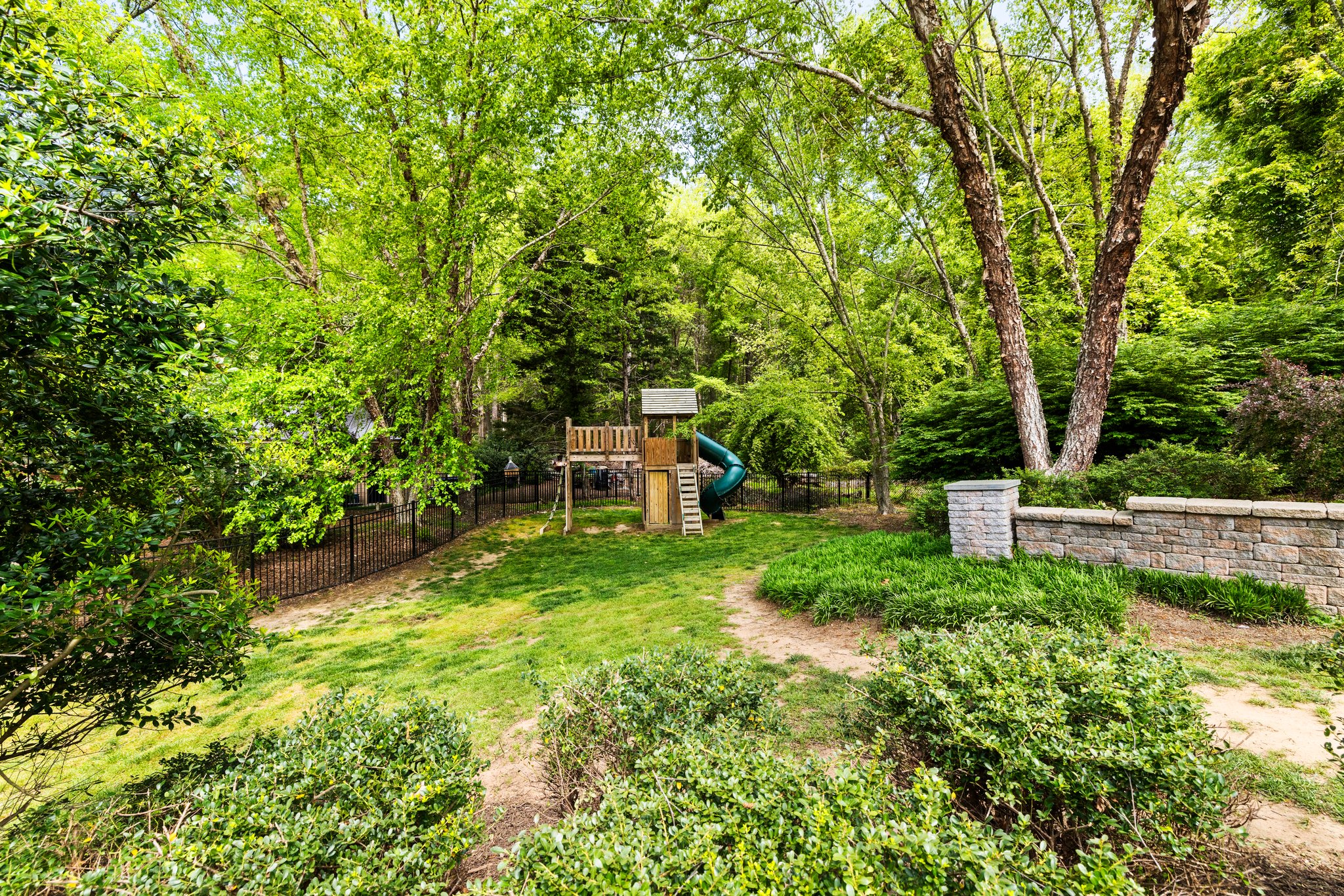 Private back yard with ornamental metal fence and playset that conveys.