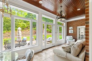 Bright sun room with heated tile floors, exposed brick walls, beaded board ceiling, and a wall of windows overlooking the private patio and backyard.
