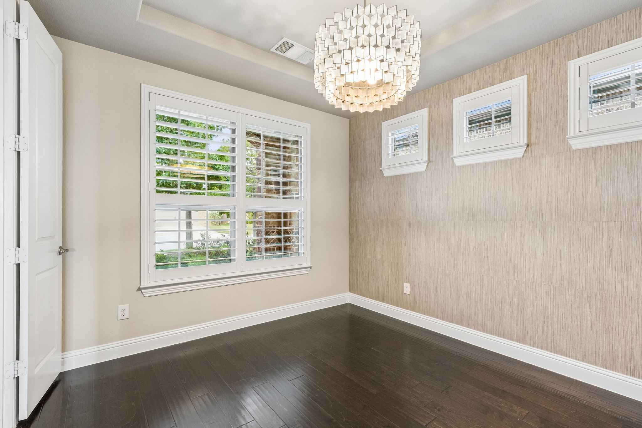 The dedicated home office pairs hardwood floors with a tray ceiling, grasscloth wallpaper accent wall and statement designer chandelier.