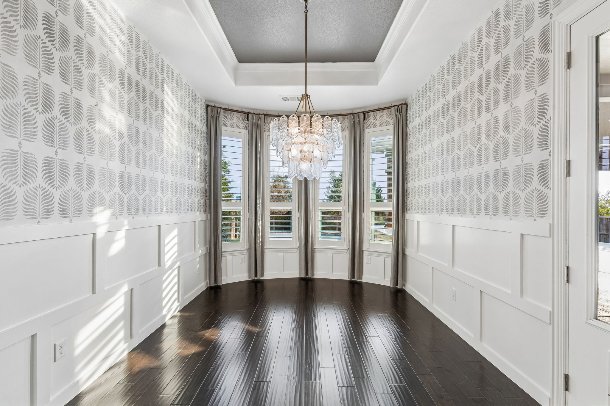 The dedicated dining room makes a statement with board-and-batten wainscoting, Serena & Lily wallpaper, custom drapery and a three-tier glass petal chandelier