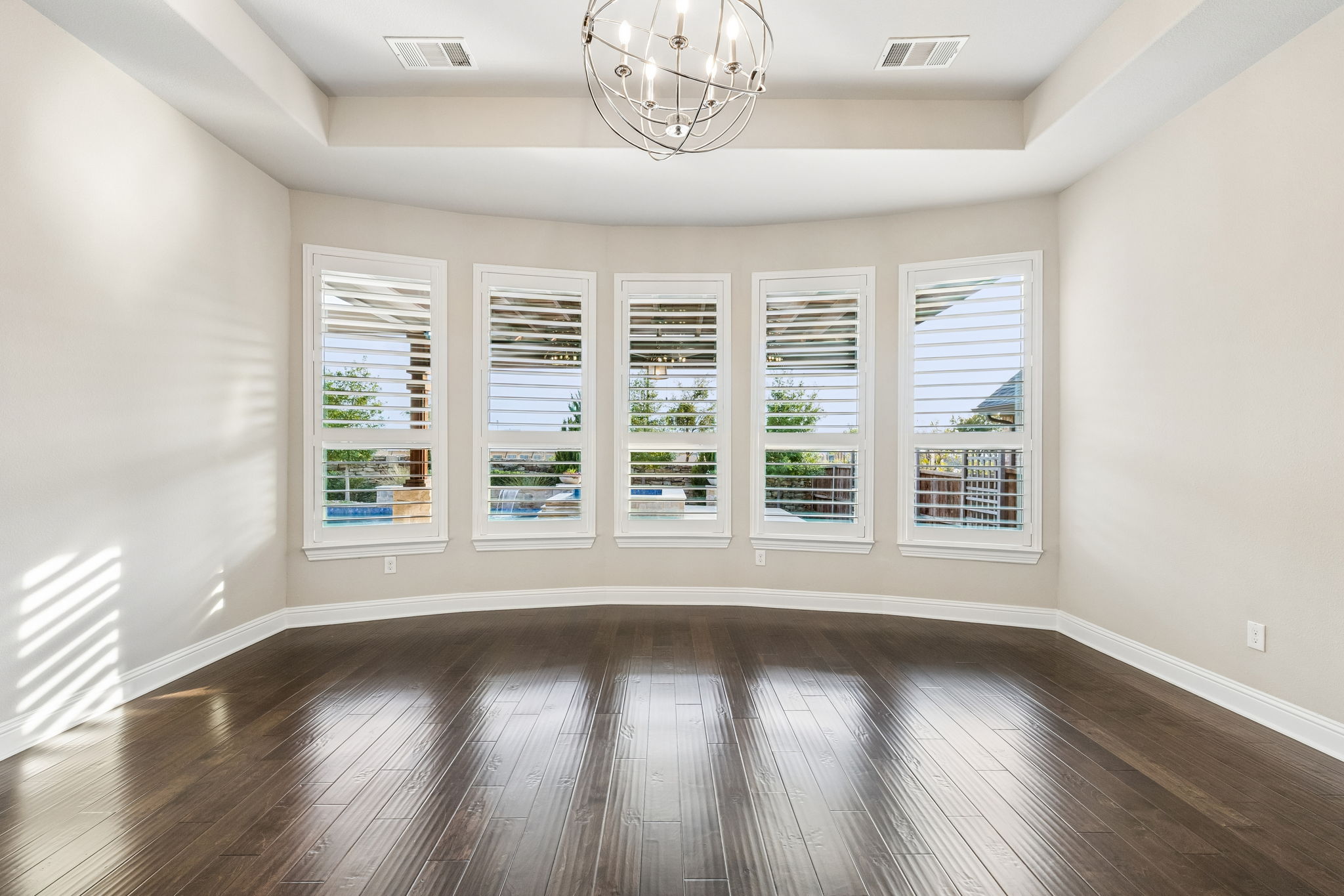 A bowed wall of plantation-shuttered windows fills the primary suite with natural light while capturing views toward the backyard and pool.