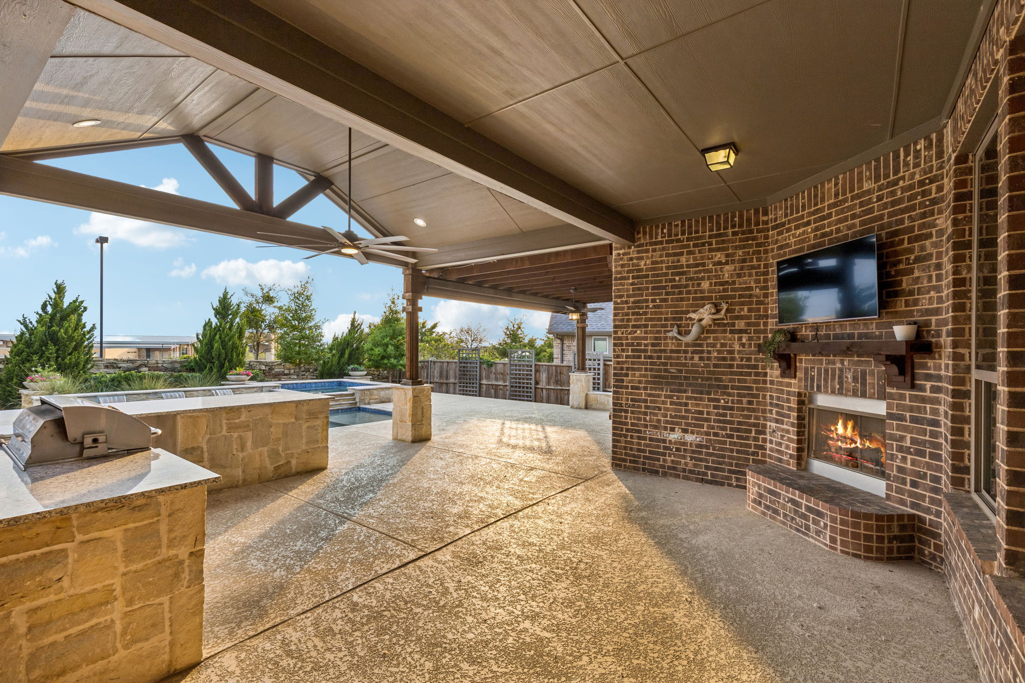 The vaulted extended patio creates a true outdoor living room with a built-in fireplace, TV and seamless views toward the pool.