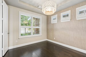 The dedicated home office pairs hardwood floors with a tray ceiling, grasscloth wallpaper accent wall and statement designer chandelier.