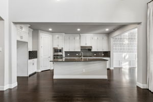 The open-concept kitchen is anchored by an expansive granite island and surrounded by ceiling-height white shaker cabinetry, stainless appliances and rich hardwood floors