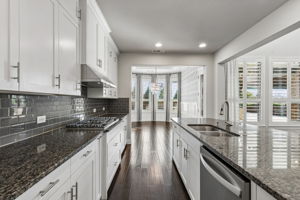 The kitchen’s granite surfaces, ceiling-height cabinetry and 2026 gas cooktop flow seamlessly into the designer-finished dining room beyond