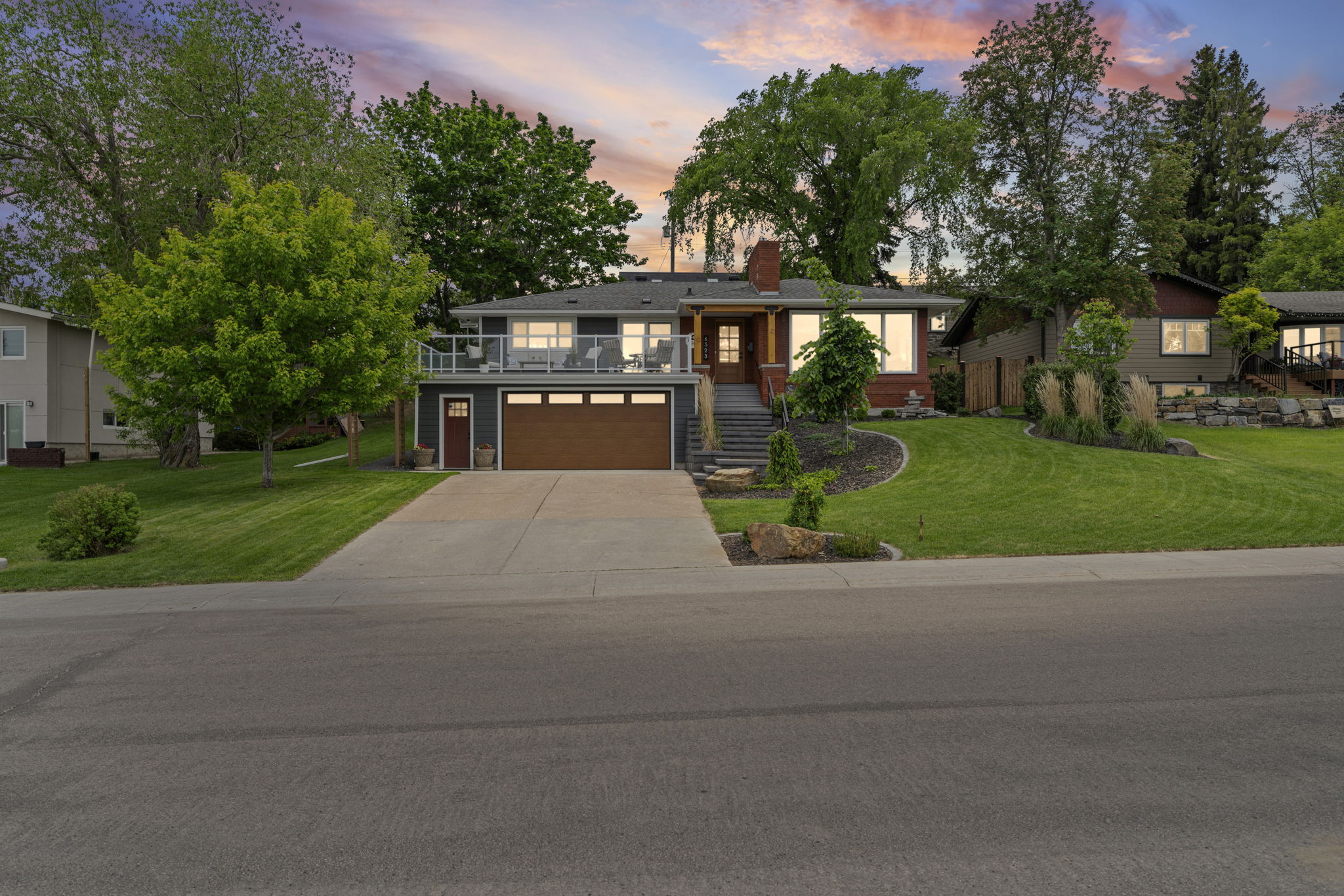 Front view of a two-storey home with a raised glass-railed terrace and attached garage at dusk.