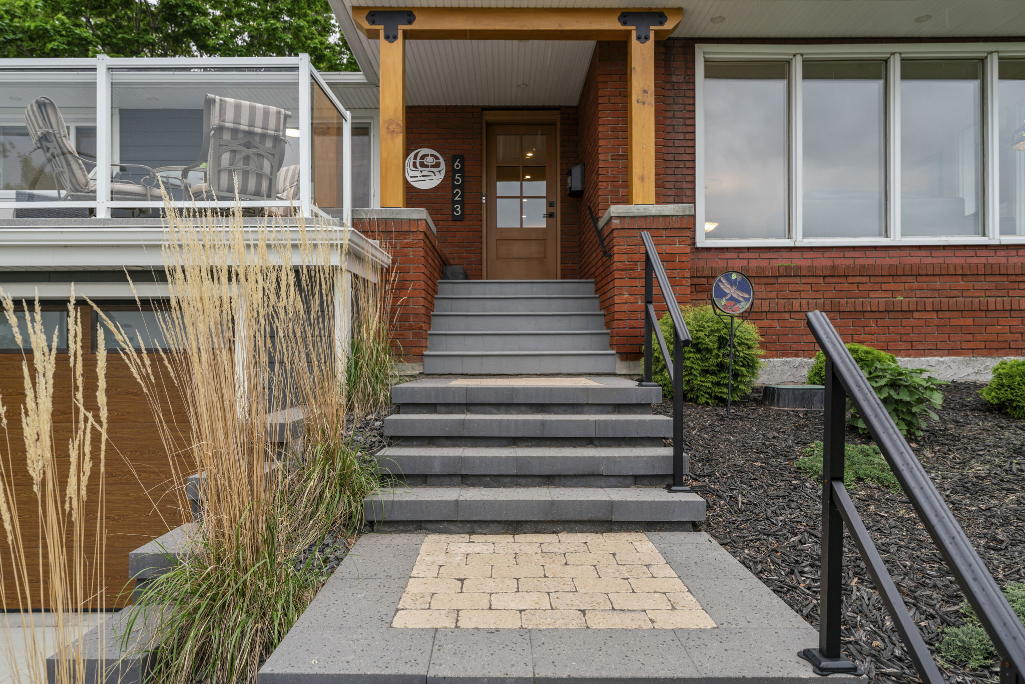 Front steps with a black handrail leading to the wood entrance door.