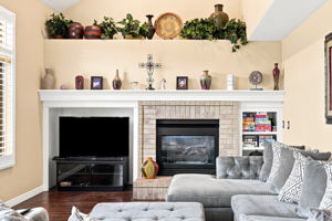 Large family room with high ceilings, fireplace, built in shelving, plant ledge, hardwood flooring, plantation shutters.