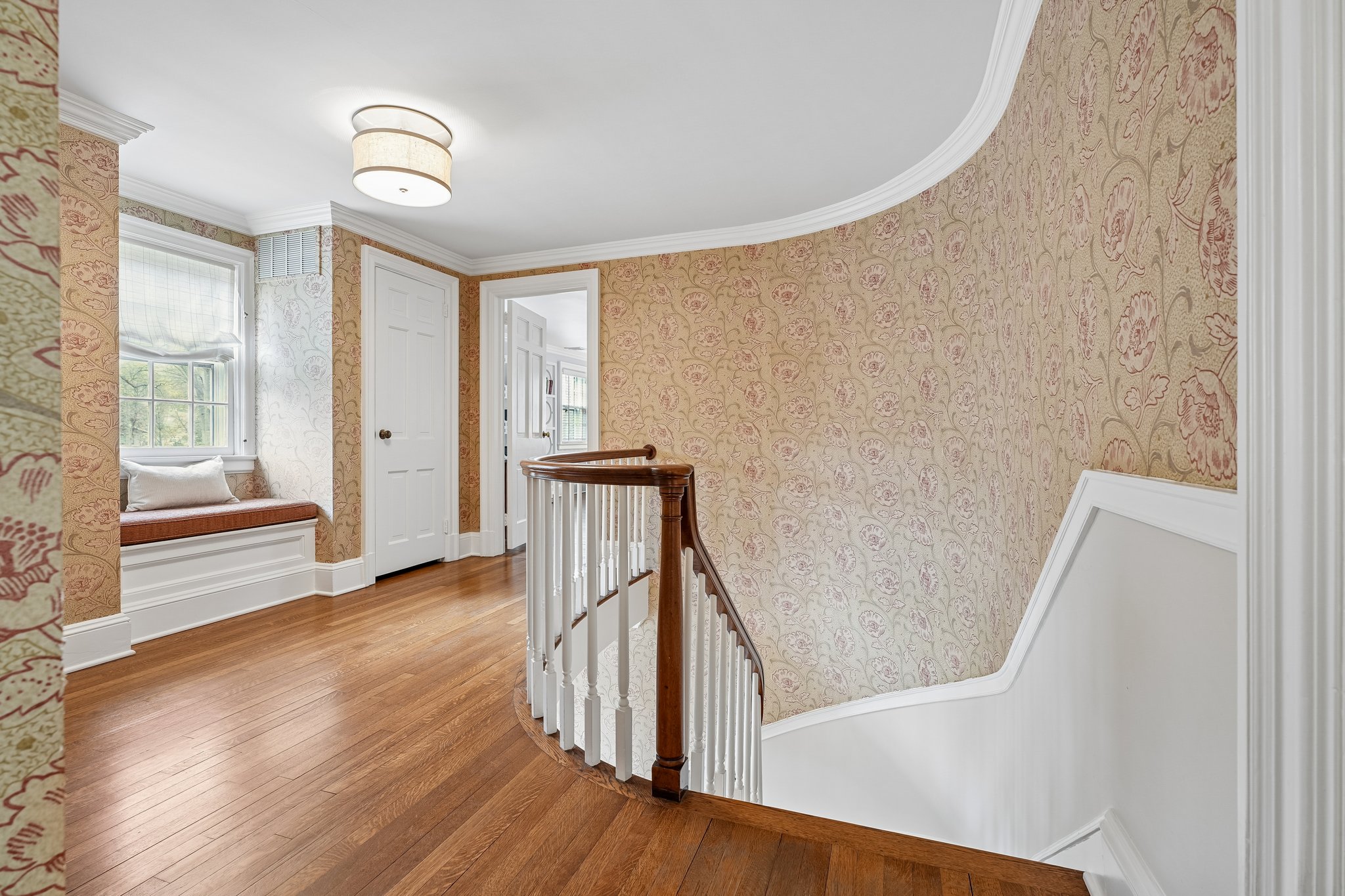 A graceful transition between levels, where a softly curved staircase and timeless wallpaper create a moment of architectural beauty that feels both classic and quietly unexpected.