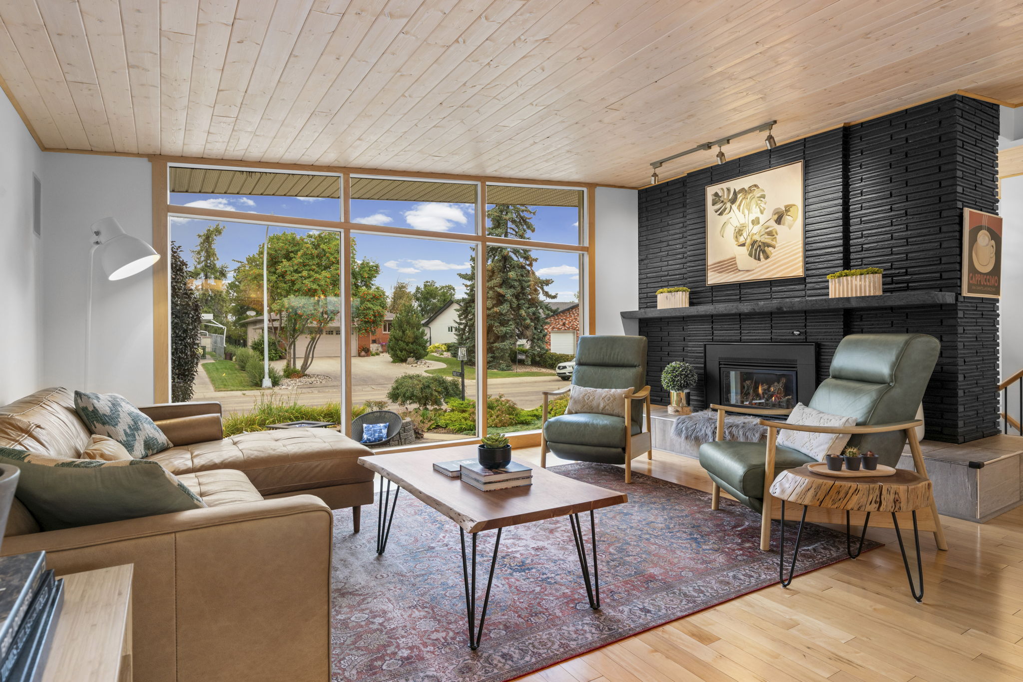 Living room with a wood ceiling, green sofa and dark fireplace beside a large window.