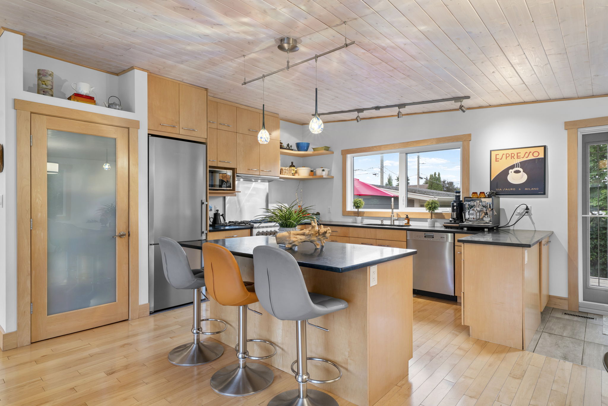 Wood-cabinet kitchen with a dark-topped island and three stools beneath pendant lights.