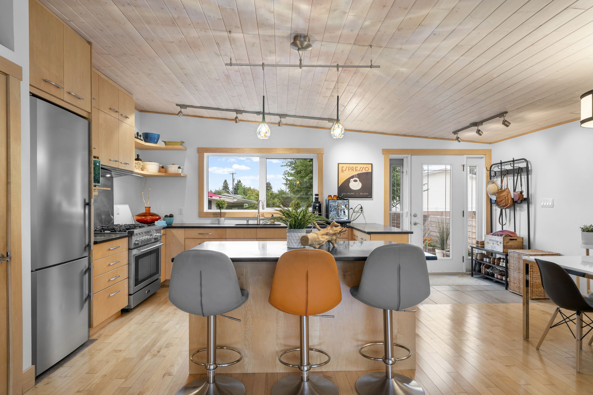 Kitchen island with grey and orange stools beside a window above the sink.