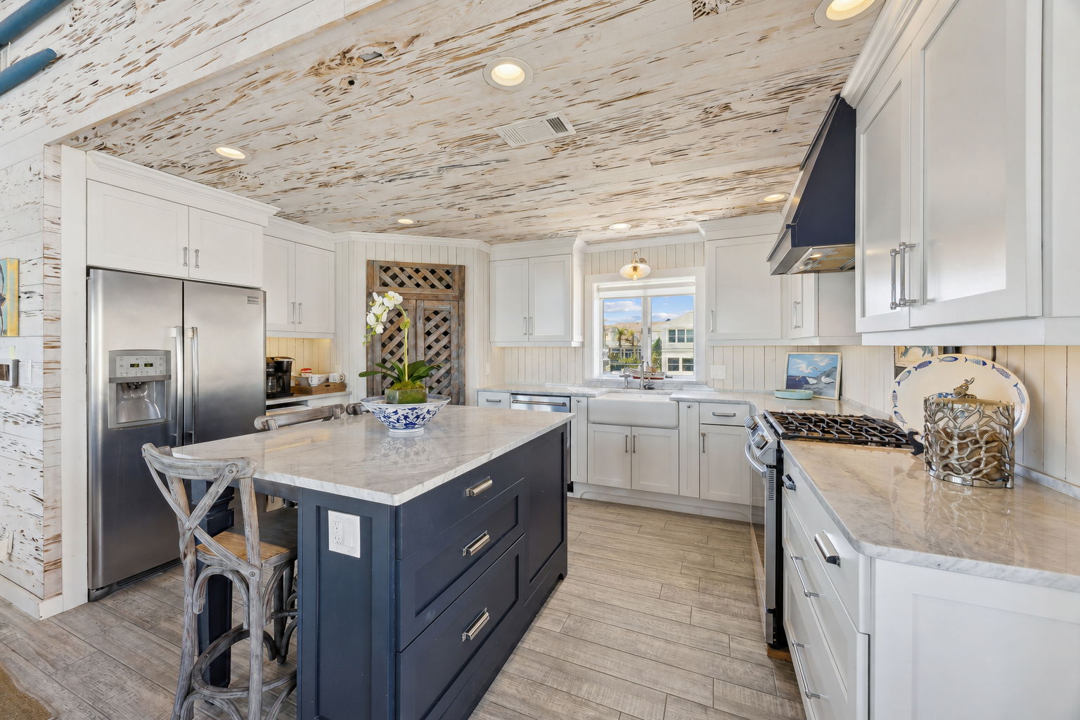 White cabinetry, quartz counters, stainless appliances, and a navy island create a crisp coastal workspace...
