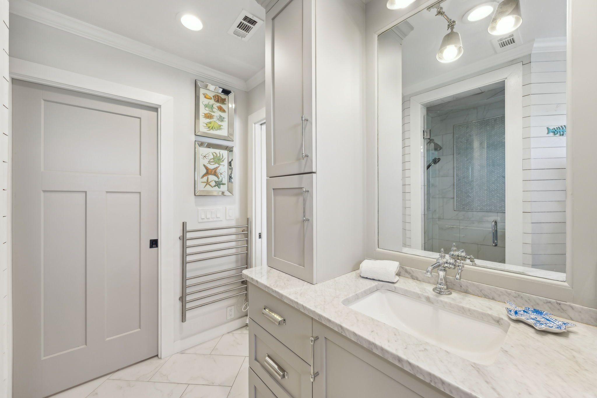 The primary bath feels bright and polished, with quartz finishes, custom cabinetry, and coastal artwork...