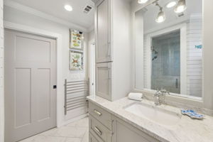 The primary bath feels bright and polished, with quartz finishes, custom cabinetry, and coastal artwork...