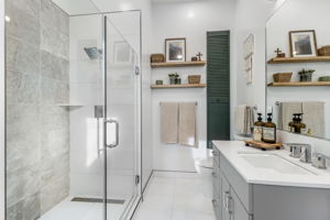 Indulge in the primary suite’s spa-like bath, complete with a walk-in shower, integrated bench, and striking limestone-accented walls. Floating shelves convey.